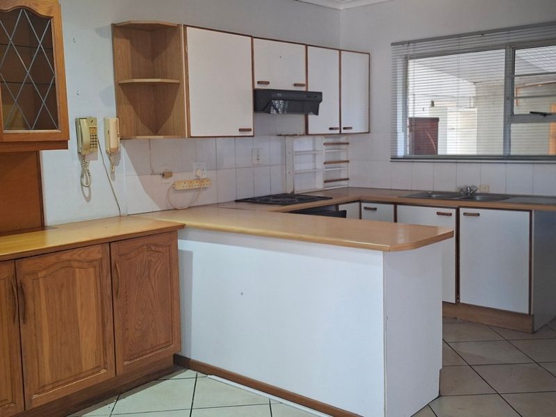 A dated kitchen featuring wooden and white cabinetry, laminate countertops, a gas hob, and tiled flooring, offering potential for a modern renovation.