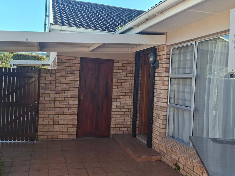 A paved outdoor patio area featuring a covered roof, brick wall construction, and direct access to the home via a timber door.