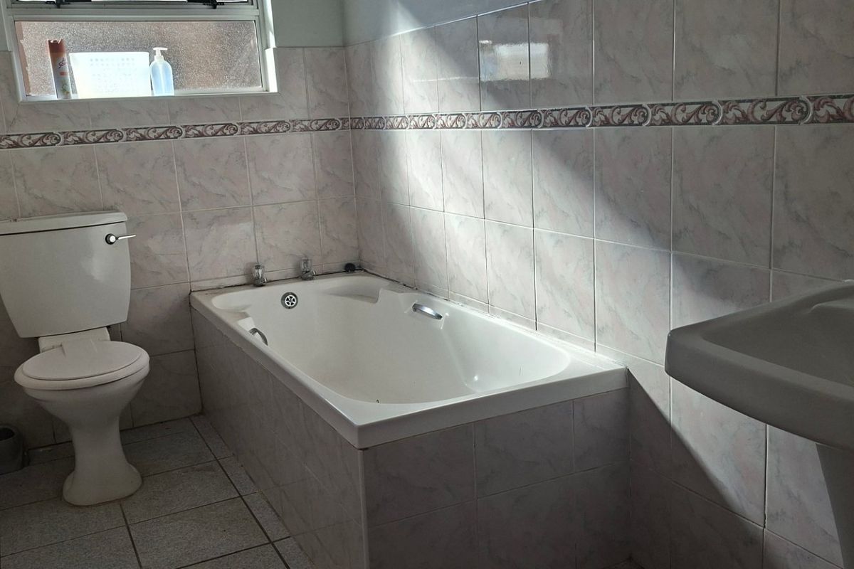 A functional bathroom featuring a built-in bathtub, pedestal basin, and toilet with tiled finishes throughout.