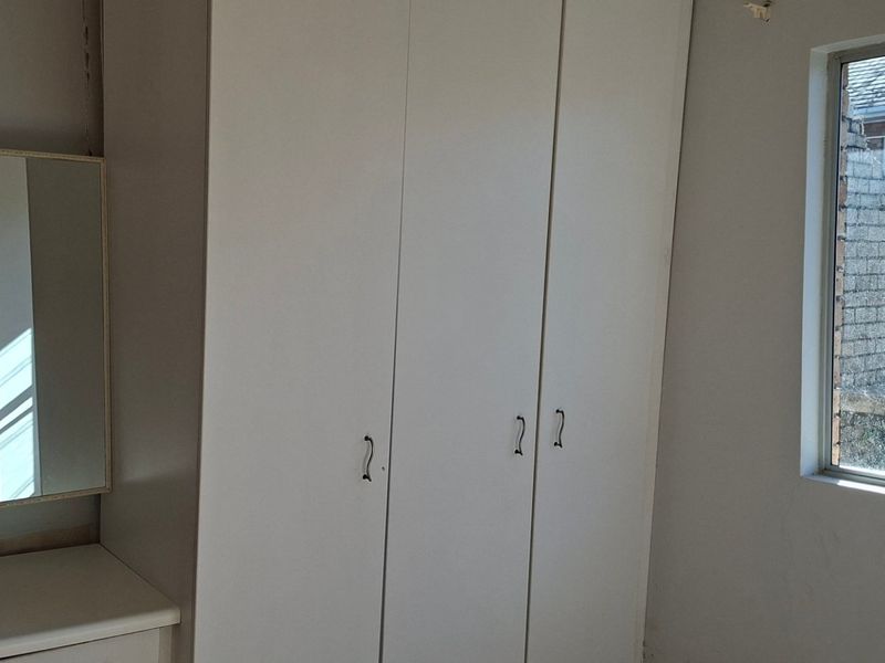 A bedroom featuring built-in cupboards and a vanity unit, with a window overlooking the exterior boundary wall.
