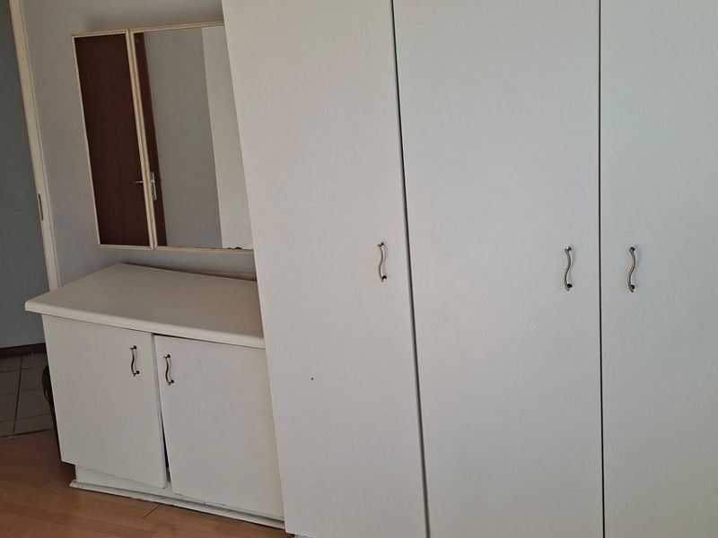 A bedroom featuring built-in cupboards and a matching vanity unit with laminate flooring, presenting a functional space ready for updates.