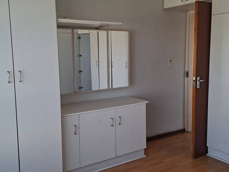 A bedroom featuring extensive built-in cupboard storage, a vanity unit with a mirror, and laminate flooring.