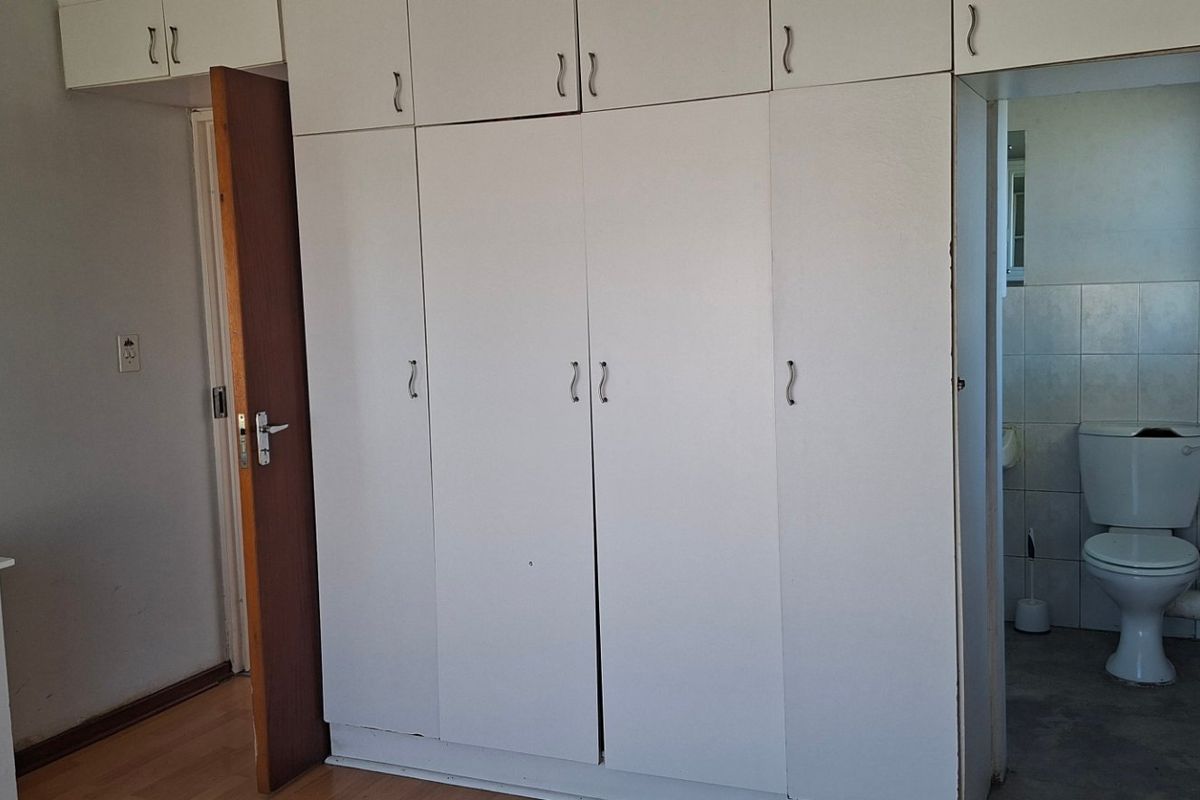 A bedroom featuring built-in cupboards and laminate flooring, with an attached en-suite bathroom containing a toilet.