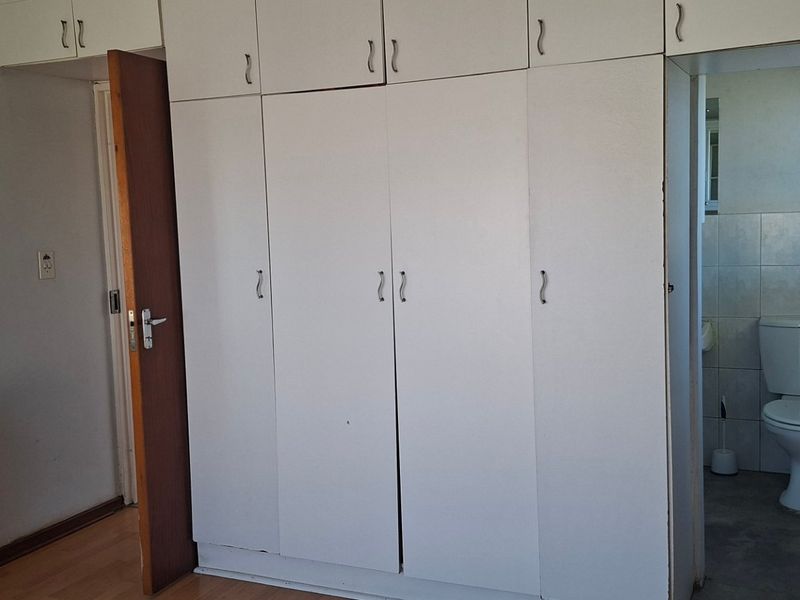 A bedroom featuring built-in cupboards and laminate flooring, with an attached en-suite bathroom containing a toilet.