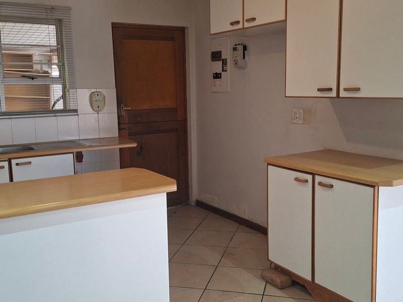 A dated kitchen featuring laminate countertops, white cabinetry, and tiled flooring, offering a functional layout ready for modern renovation.