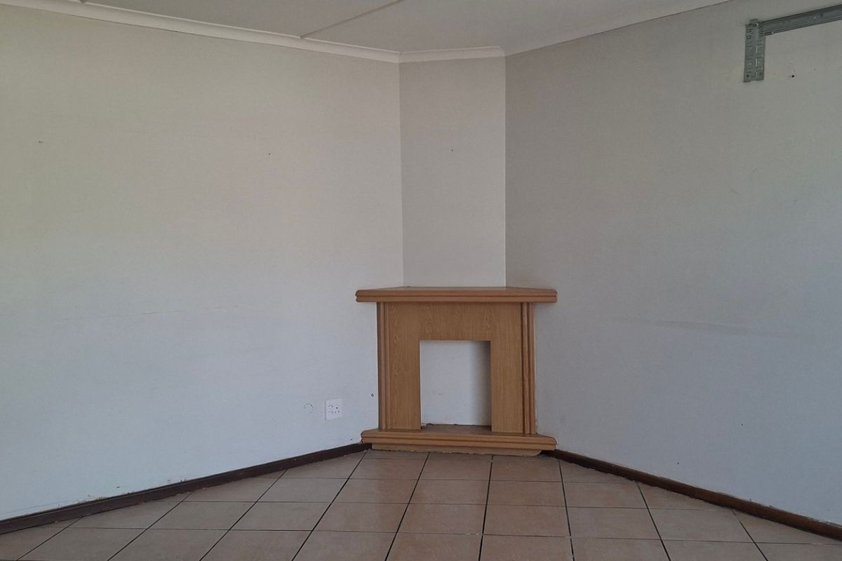 An empty living room featuring ceramic floor tiles, a corner fireplace mantel, and a wall-mounted bracket for an air conditioning unit.