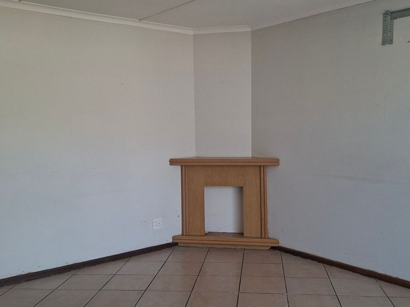 An empty living room featuring ceramic floor tiles, a corner fireplace mantel, and a wall-mounted bracket for an air conditioning unit.