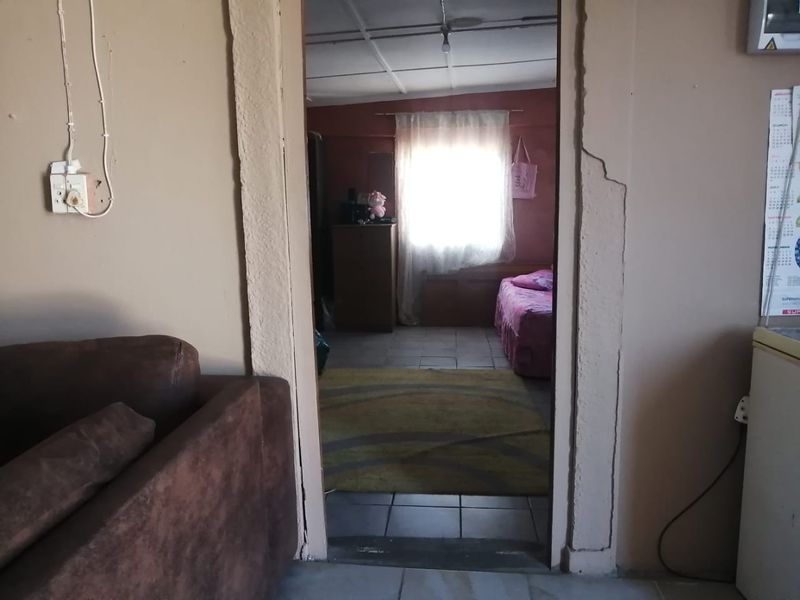 A view through a doorway into a bedroom featuring tiled flooring and a window, showing signs of wall plaster damage and exposed wiring.