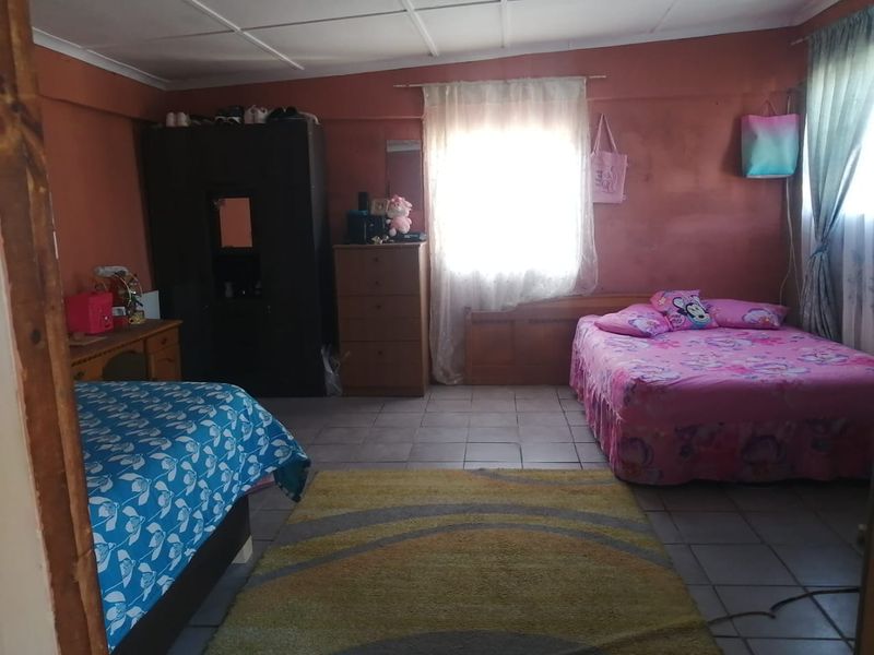 A bedroom featuring tiled flooring and ceiling panels, currently utilized with multiple beds and storage units.