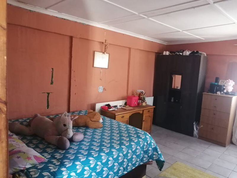 A bedroom featuring tiled flooring and exposed ceiling panels, currently showing significant wear to the wall finishes and plaster.
