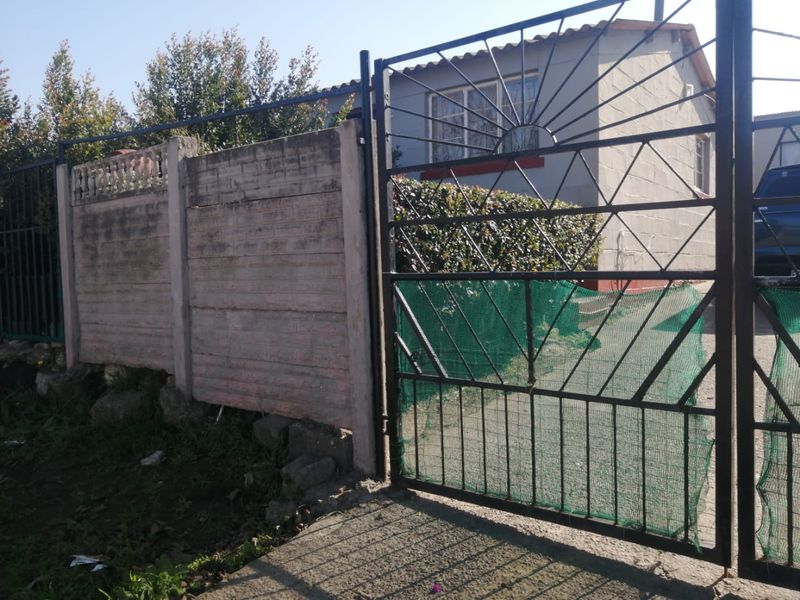 Front view of the property featuring a metal driveway gate, precast concrete boundary wall, and a tiled roof house exterior.