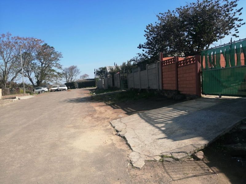 Street view showing the property boundary, including a concrete and brick wall, metal gate, and the adjacent road and driveway access.