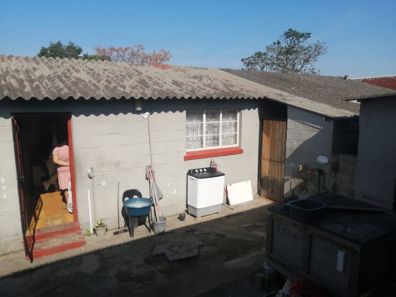 Rear exterior view of the property featuring concrete block walls, a corrugated roof, and a paved outdoor utility area.