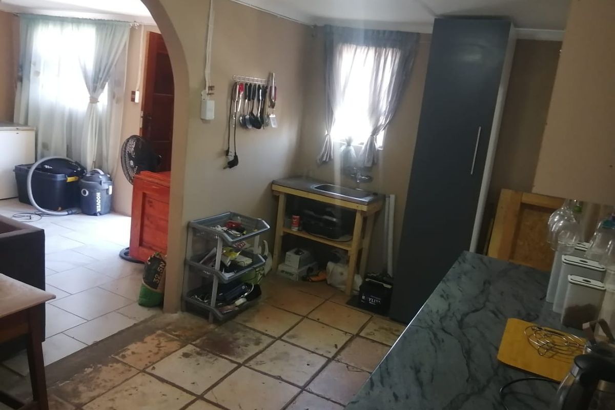 A kitchen area featuring tiled flooring, a sink unit, and a built-in pantry cupboard, connected to an adjacent room via an arched doorway.