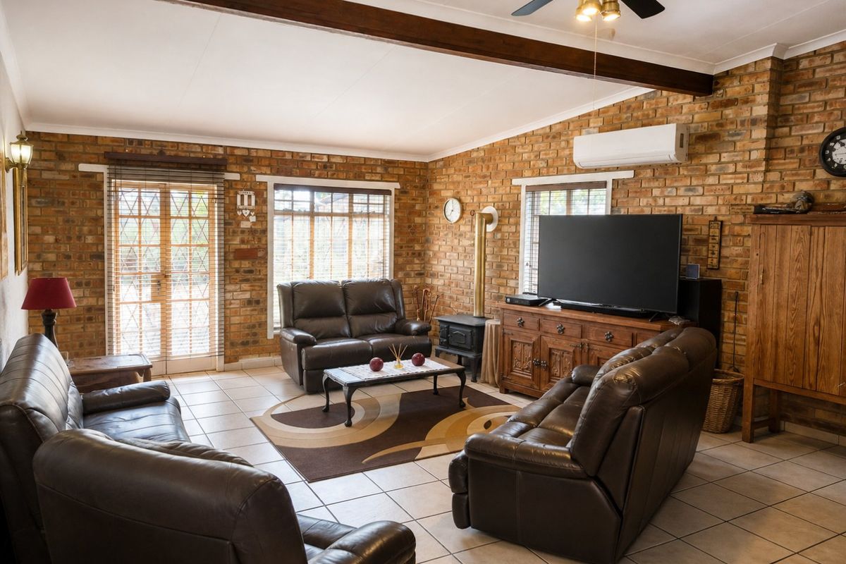 Spacious living room featuring exposed brick walls, ceramic tile flooring, a wood-burning fireplace, and a ceiling fan, with direct access to the exterior.