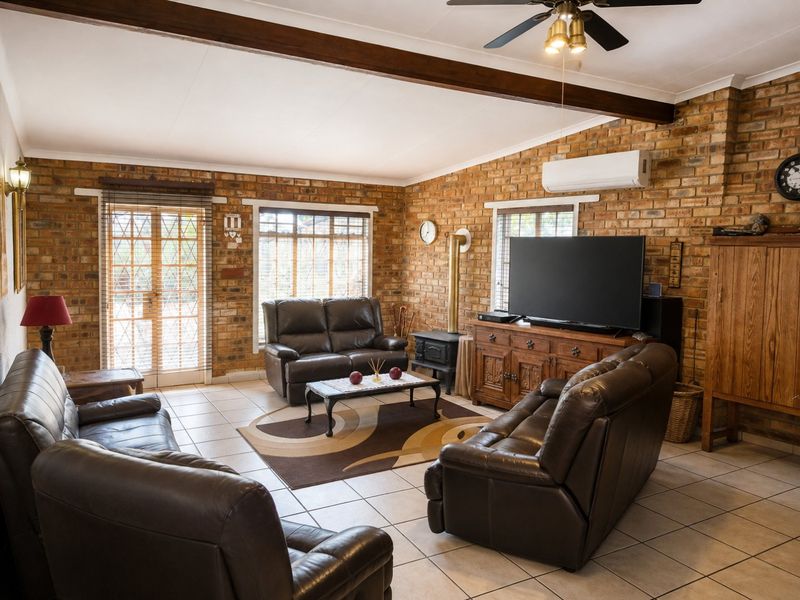 Spacious living room featuring exposed brick walls, ceramic tile flooring, a wood-burning fireplace, and a ceiling fan, with direct access to the exterior.