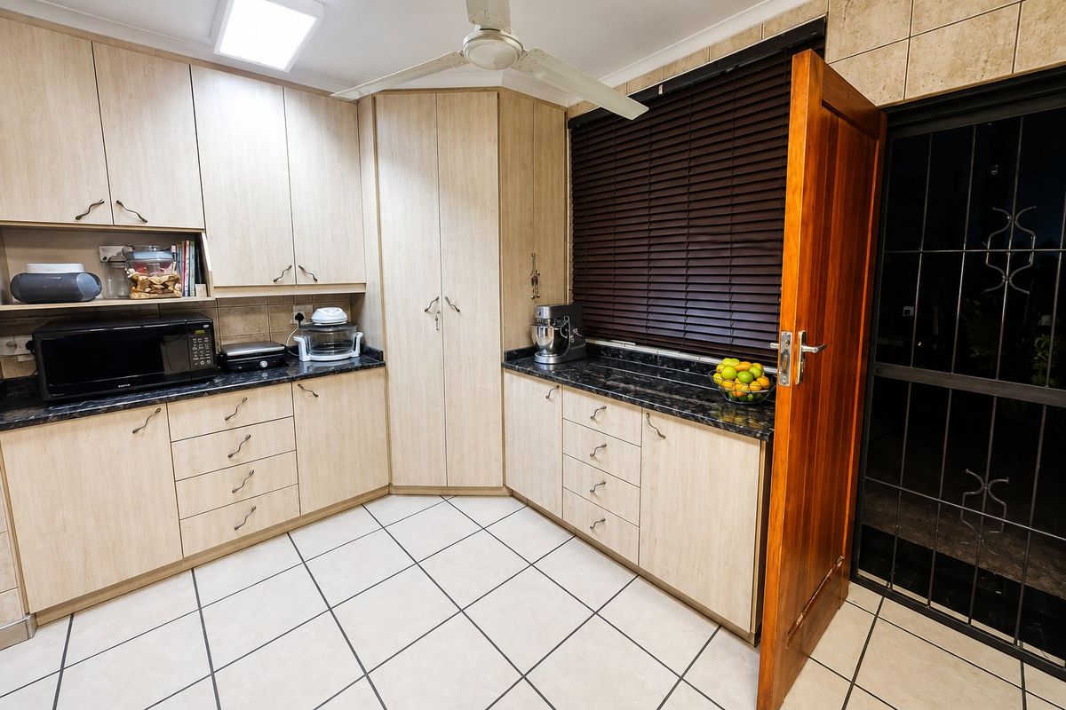 Functional kitchen featuring light wood-tone cabinetry, dark granite countertops, tiled flooring, and a ceiling fan, with direct access to an exterior security gate.
