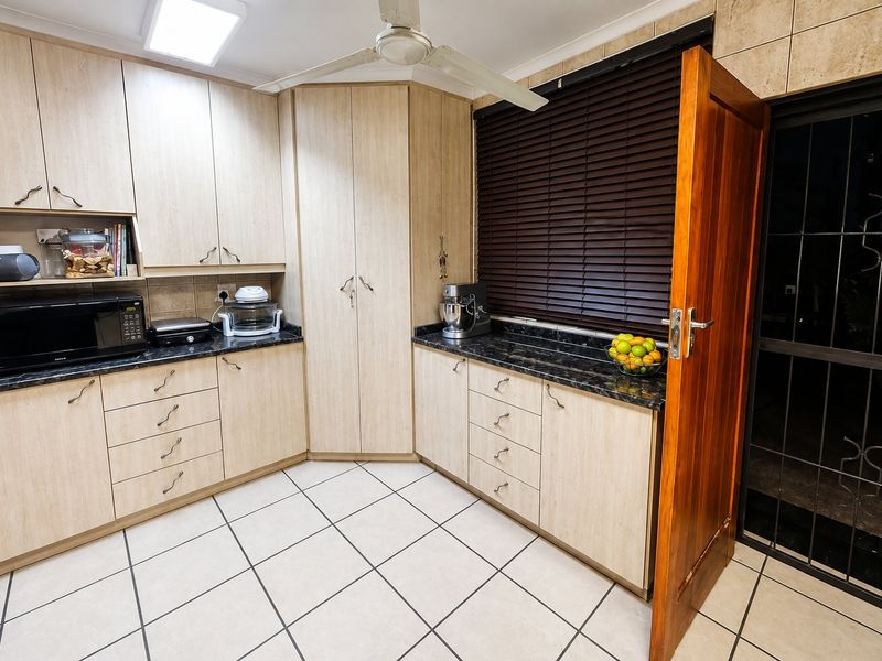 Functional kitchen featuring light wood-tone cabinetry, dark granite countertops, tiled flooring, and a ceiling fan, with direct access to an exterior security gate.