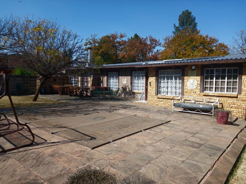 Rear exterior view featuring a paved patio area, swimming pool with cover, and a single-story brick house with a metal roof.