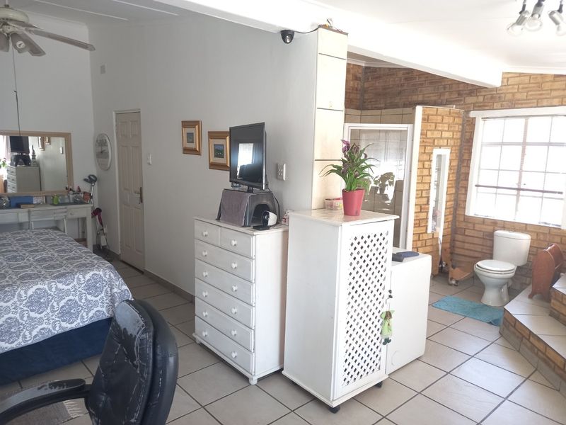 A bedroom featuring tiled flooring, an exposed brick wall, and an integrated en-suite bathroom area with a toilet.