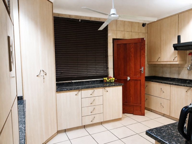 A functional kitchen featuring light wood cabinetry, dark granite countertops, tiled flooring, and a ceiling fan, providing ample storage and workspace.