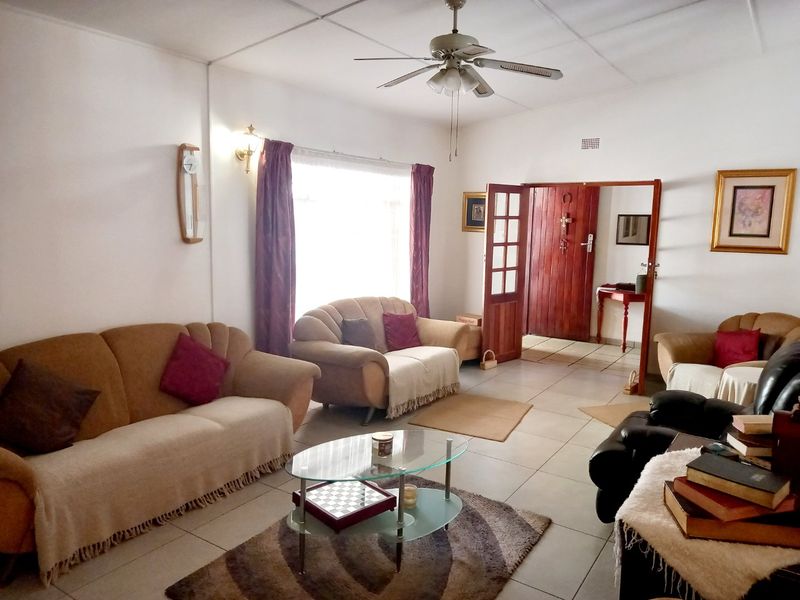 A spacious living room featuring tiled flooring, a ceiling fan, and a timber entrance door, offering a functional and well-lit living space.
