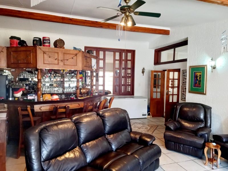 A spacious entertainment area featuring a built-in wooden bar, exposed timber ceiling beams, and tiled flooring, offering a classic and functional social space.