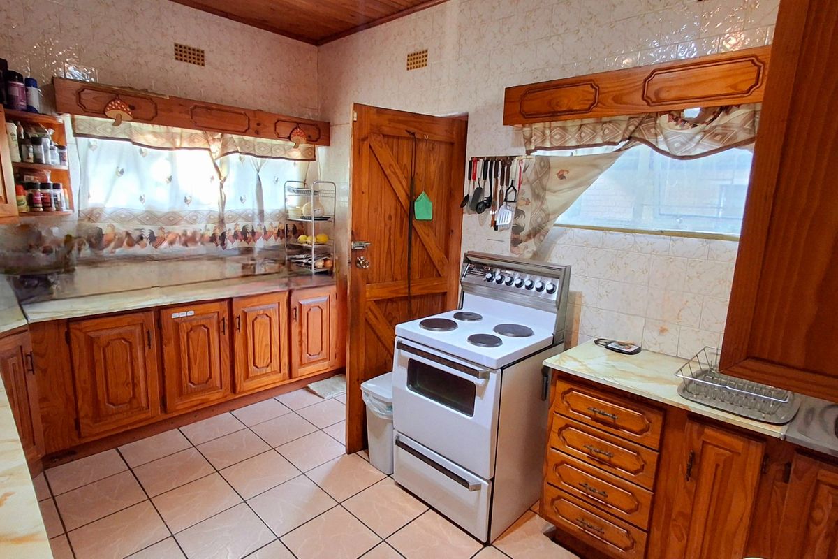 A functional kitchen featuring traditional wooden cabinetry, tiled splashbacks, and a freestanding stove, offering a classic layout with potential for modern updates.