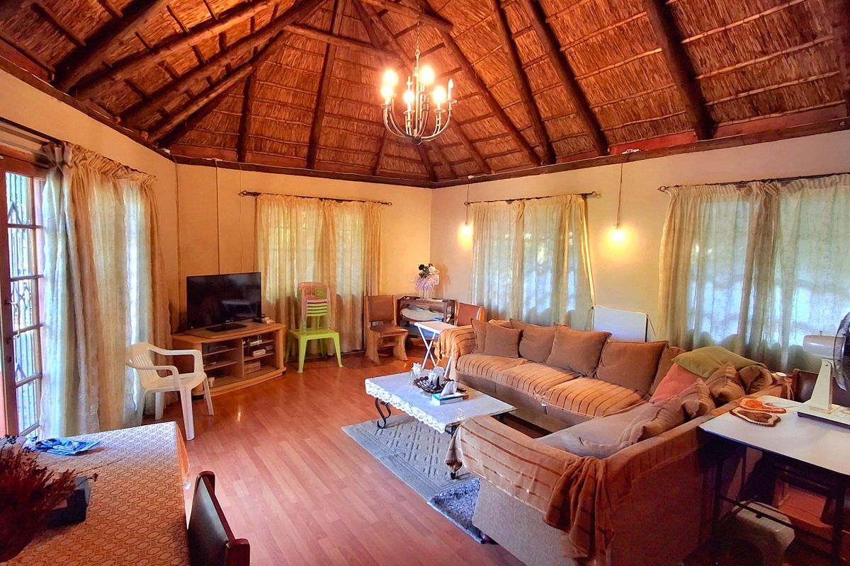 Spacious living room featuring a high vaulted thatched ceiling with exposed timber rafters, laminate flooring, and large sliding doors providing access to the outdoors.