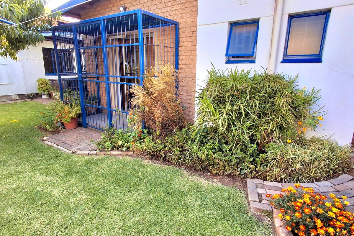 Rear garden area featuring a lawn, brick paved pathway, and a secure metal gate enclosure attached to the brick exterior wall.