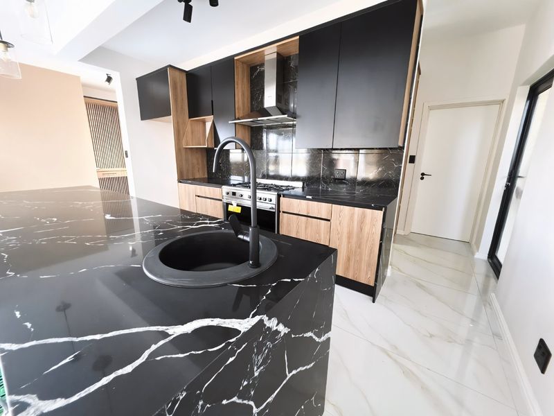 Modern kitchen featuring a striking black marble-look stone island, integrated gas hob, stainless steel extractor, and sleek two-tone cabinetry with high-end finishes.