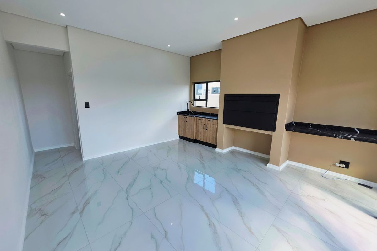 A modern, open-plan living area featuring polished marble-look floor tiles, a built-in fireplace, and a convenient kitchenette corner with stone countertops.