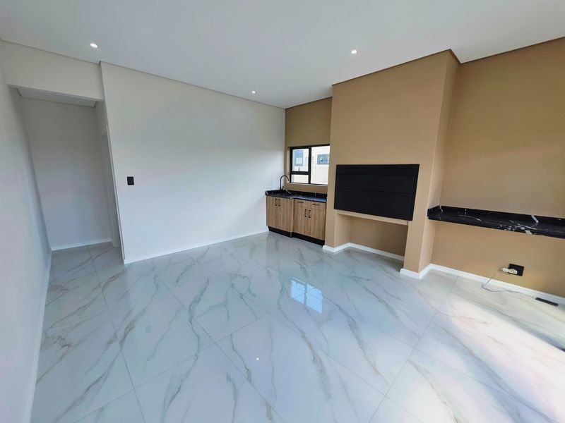 A modern, open-plan living area featuring polished marble-look floor tiles, a built-in fireplace, and a convenient kitchenette corner with stone countertops.