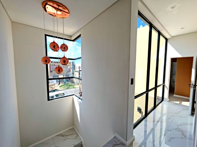 A bright, modern hallway featuring large format marble-look floor tiles, expansive black-framed windows, and a contemporary copper pendant light fixture.