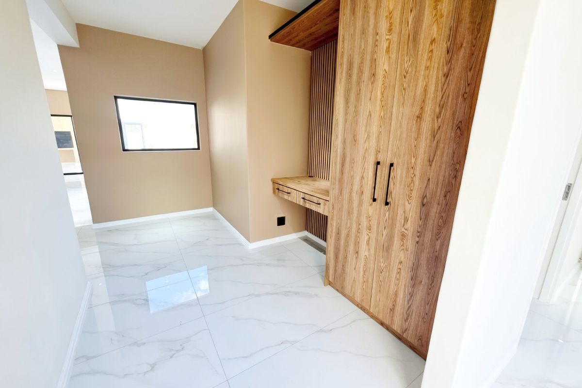 A modern bedroom featuring high-quality marble-look floor tiles, a custom built-in wardrobe, and an integrated timber desk with slatted wall detailing.