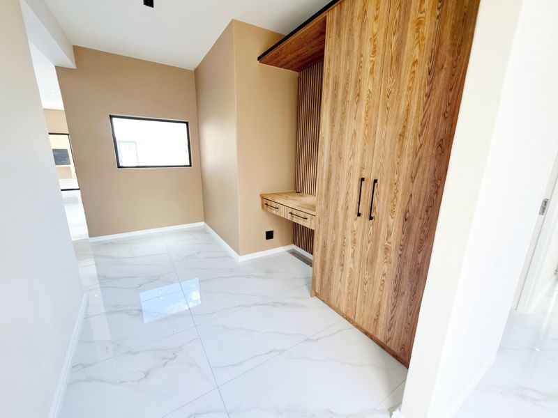 A modern bedroom featuring high-quality marble-look floor tiles, a custom built-in wardrobe, and an integrated timber desk with slatted wall detailing.