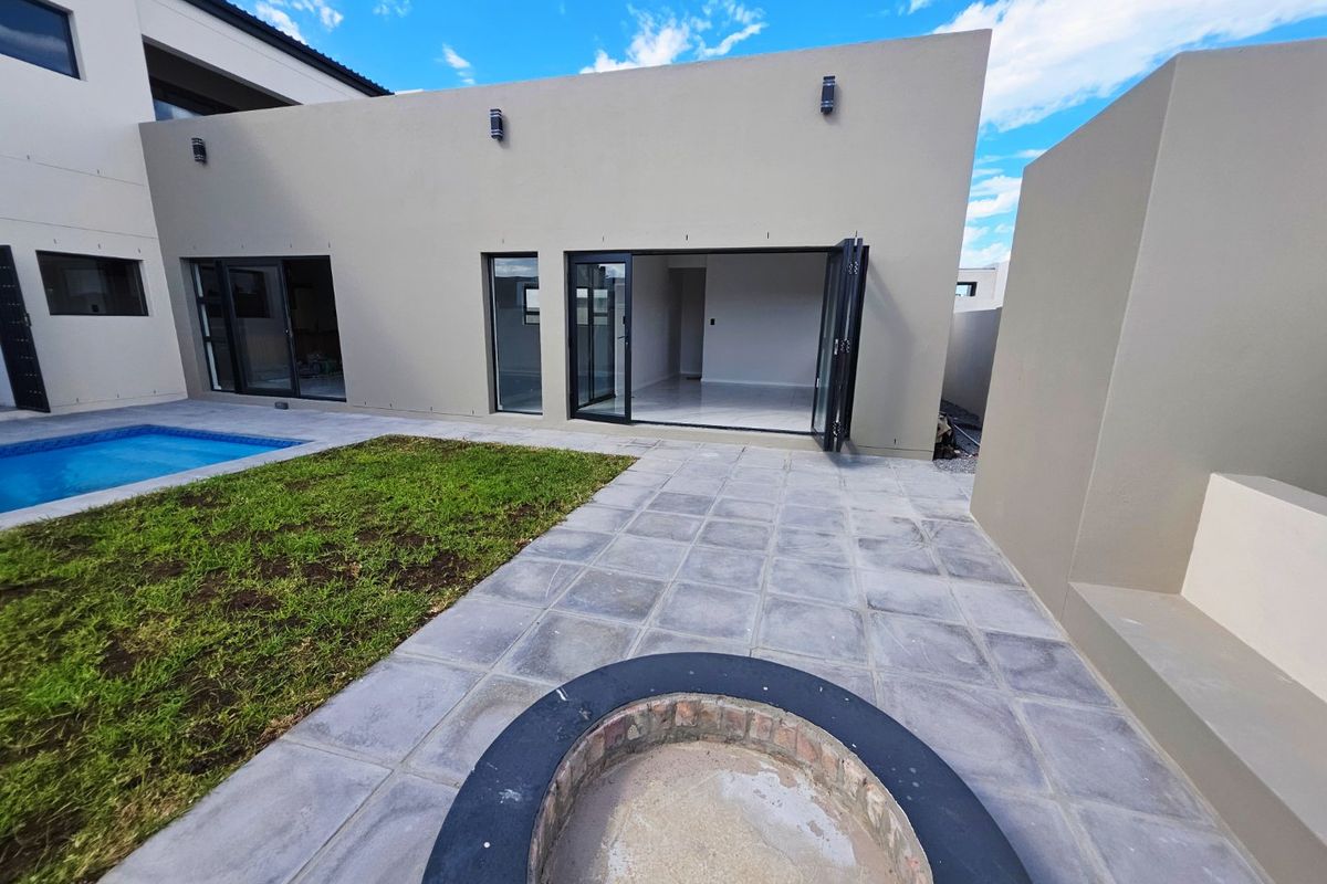 Modern rear exterior featuring a tiled patio, built-in fire pit, swimming pool, and bi-fold doors leading into the home.