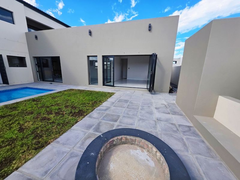 Modern rear exterior featuring a tiled patio, built-in fire pit, swimming pool, and bi-fold doors leading into the home.