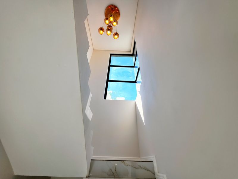 A bright and modern stairwell featuring a contemporary multi-pendant light fixture and a large window providing ample natural light.