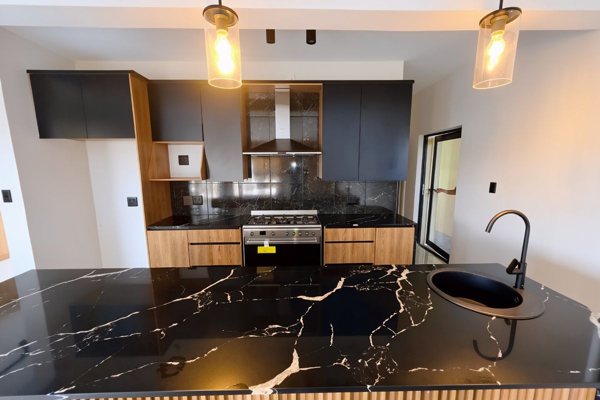 Modern kitchen featuring high-contrast black marble-effect countertops, two-tone cabinetry, built-in gas stove, and a sleek black undermount sink with a matching gooseneck faucet.