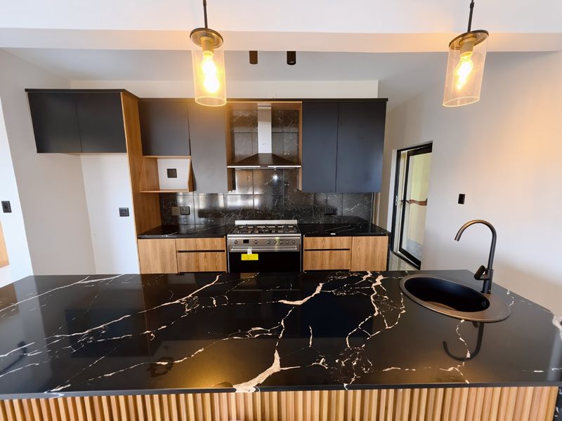 Modern kitchen featuring high-contrast black marble-effect countertops, two-tone cabinetry, built-in gas stove, and a sleek black undermount sink with a matching gooseneck faucet.