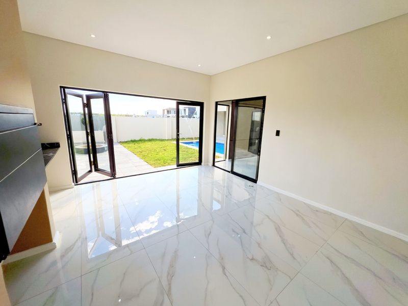 Spacious, modern living area featuring high-gloss marble-look floor tiles, recessed lighting, and large bifold doors opening onto a private garden and pool area.