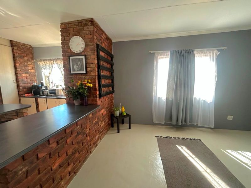 Open plan living area featuring an exposed brick wall, breakfast bar, and kitchen cabinetry, creating a functional and connected space.