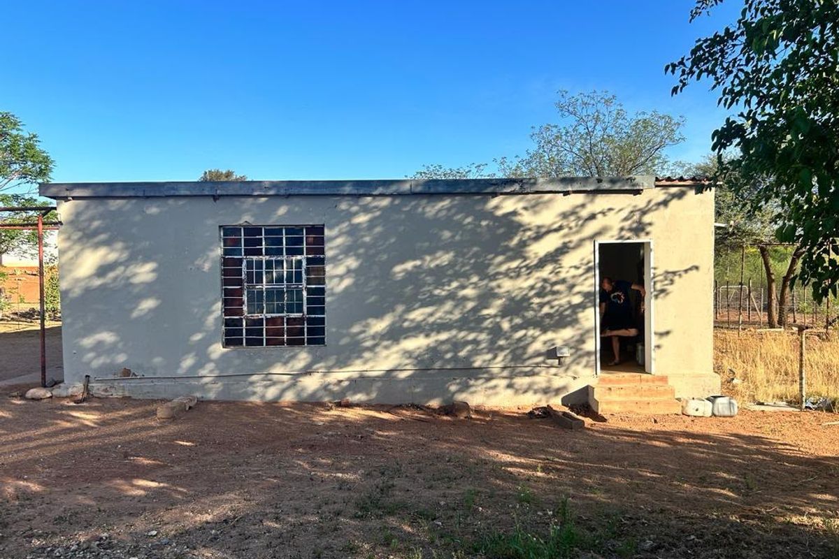 Rear view of a single-story residential structure featuring a simple facade, security-barred window, and concrete entrance steps.