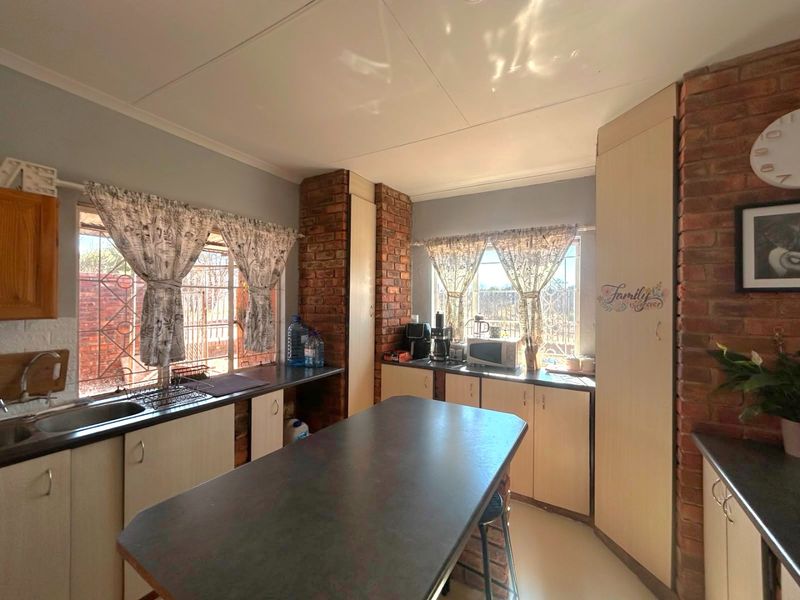 A functional kitchen featuring exposed brick accents, laminate countertops, built-in cabinetry, and large windows with security bars.