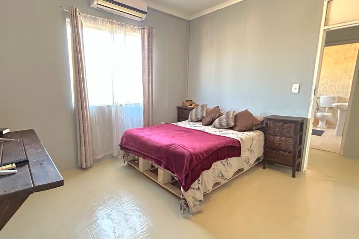 A bedroom featuring painted concrete floors, a wall-mounted air conditioning unit, and direct access to an en-suite bathroom.