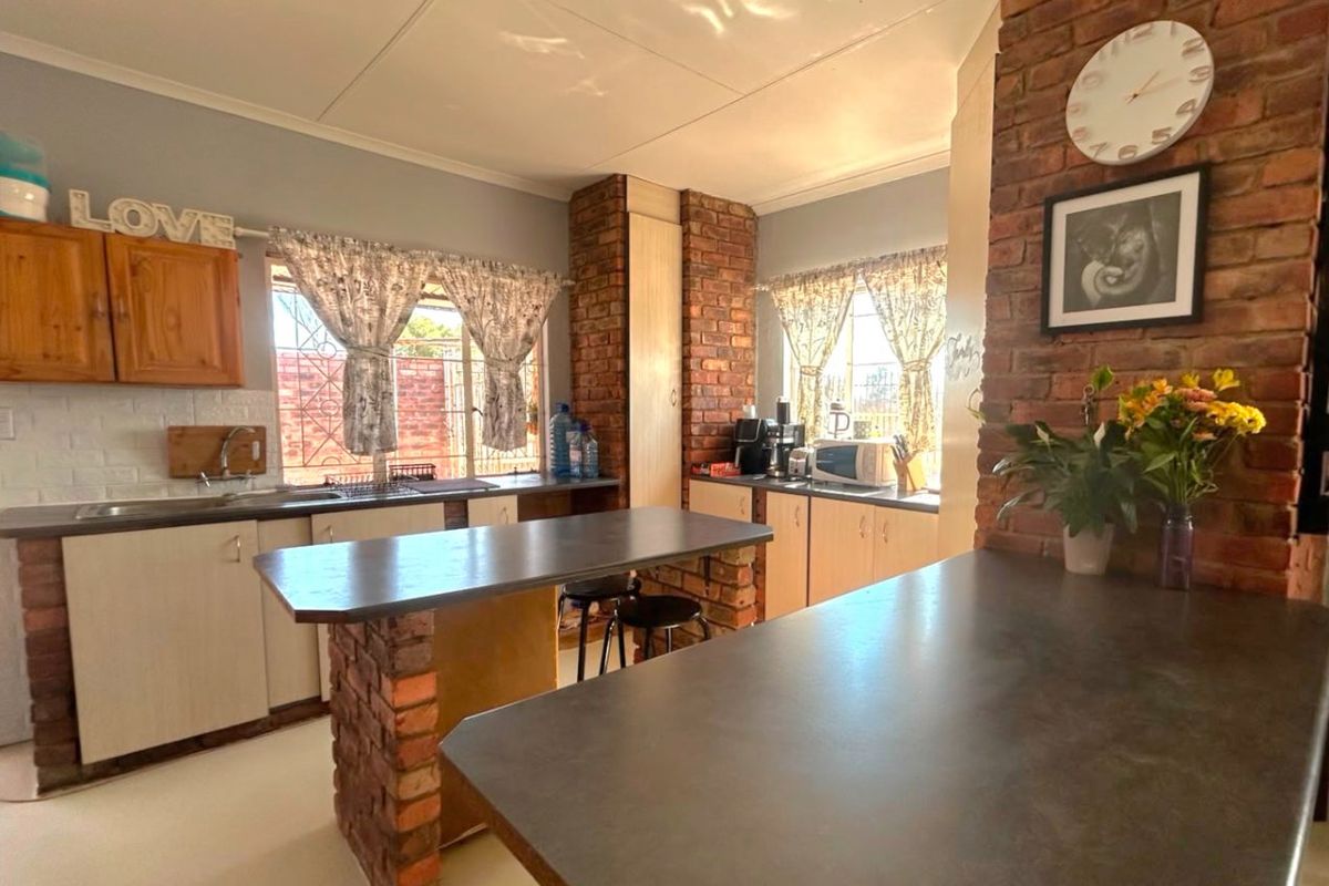 A rustic-style kitchen featuring exposed brick structural pillars, ample built-in cabinetry, laminate countertops, and a functional layout with a central breakfast bar.