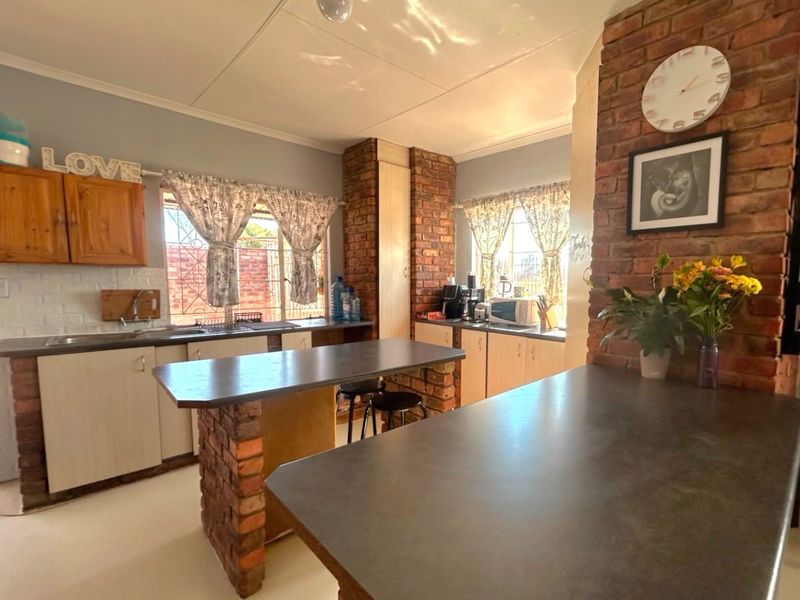 A rustic-style kitchen featuring exposed brick structural pillars, ample built-in cabinetry, laminate countertops, and a functional layout with a central breakfast bar.