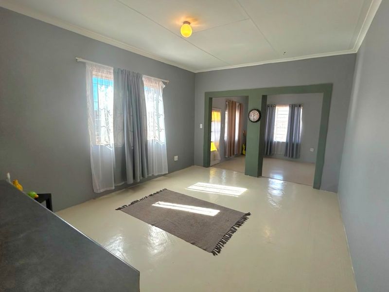 Spacious open-plan living area featuring neutral grey walls, painted concrete flooring, and large windows with security bars, offering a versatile layout.