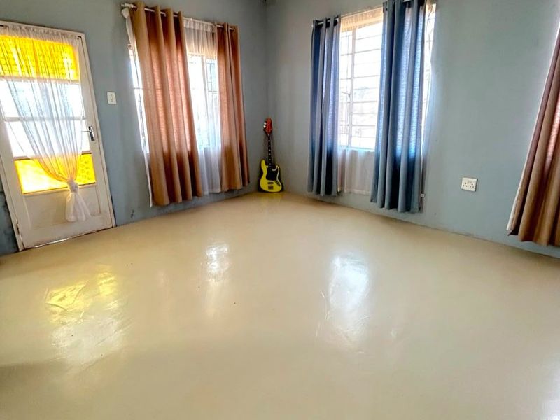 A spacious, empty living room featuring painted concrete floors, large windows with security bars, and a glass panel door leading outside.
